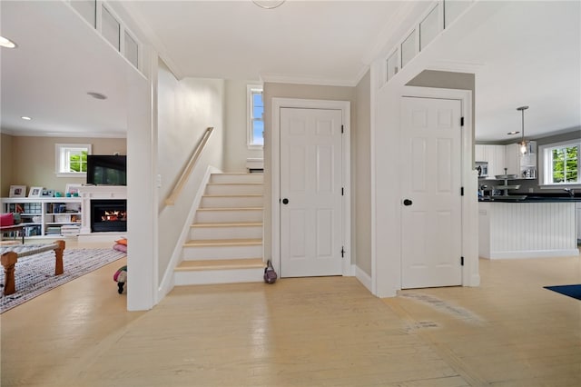 9 Casey Ct, Newport, RI 02840 - foyer entrance featuring crown molding, stairway, a lit fireplace, light wood-type flooring, and baseboards
