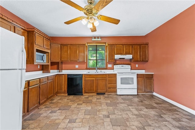 kitchen with white appliances, under cabinet range hood, a sink, brown cabinets, and light stone finish floors