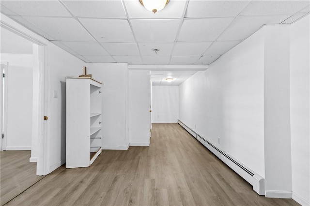 basement featuring a baseboard radiator, a drop ceiling, wood finished floors, and baseboards