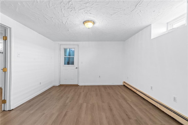 spare room with baseboard heating, light wood-type flooring, a textured ceiling, and baseboards