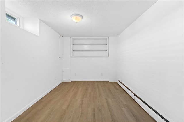 empty room with a baseboard heating unit, wood finished floors, a textured ceiling, and baseboards
