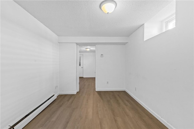 below grade area featuring baseboard heating, wood finished floors, a textured ceiling, and baseboards