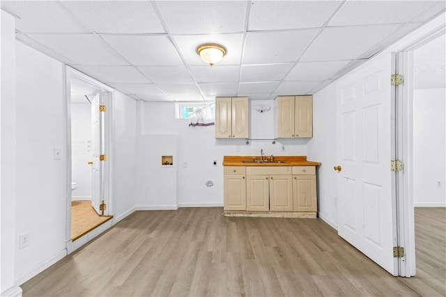 kitchen featuring a paneled ceiling, light wood-type flooring, a sink, baseboards, and butcher block counters