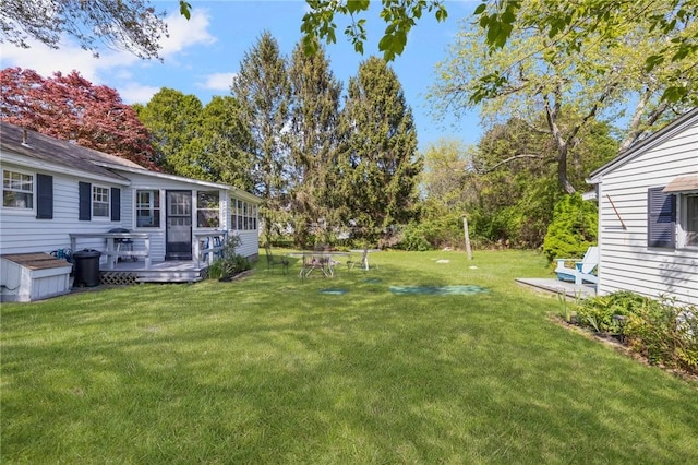 view of grassy yard featuring a deck, a sunroom, and view of scattered trees