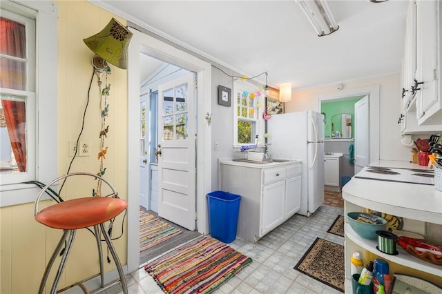 kitchen with freestanding refrigerator, white cabinets, light countertops, light flooring, and ornamental molding