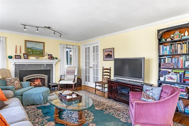 living area with a tiled fireplace, wood finished floors, french doors, and ornamental molding