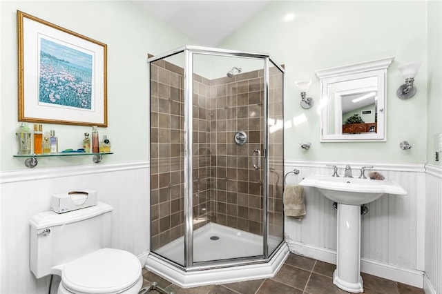 full bath featuring a stall shower, a wainscoted wall, tile patterned floors, toilet, and a sink