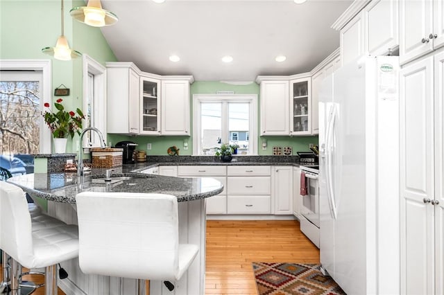 kitchen featuring white appliances, a peninsula, a breakfast bar, white cabinets, and a sink