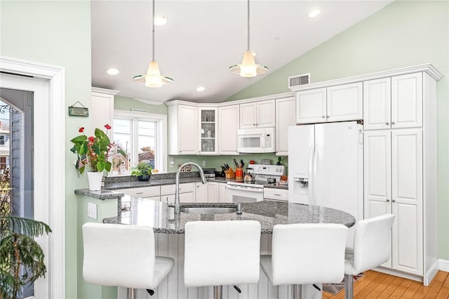 kitchen with white appliances, a sink, lofted ceiling, dark stone countertops, and decorative light fixtures