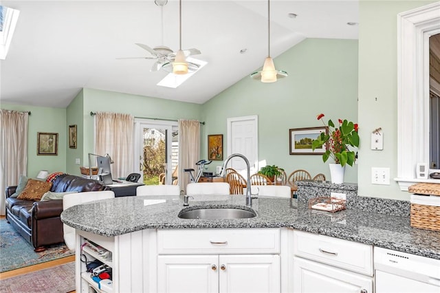 kitchen with a sink, a skylight, white dishwasher, ceiling fan, and vaulted ceiling
