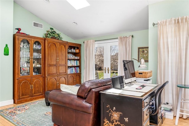 office space featuring lofted ceiling, light wood-style flooring, french doors, and a skylight