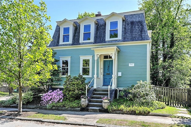second empire-style home featuring mansard roof, fence, a shingled roof, and a chimney