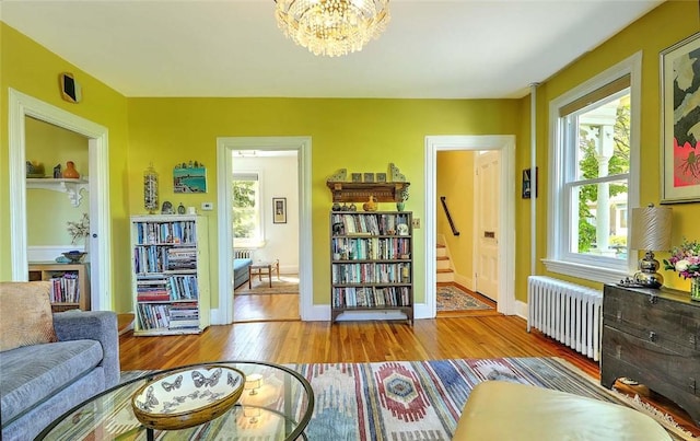 sitting room with radiator, light wood-style floors, stairway, a chandelier, and baseboards