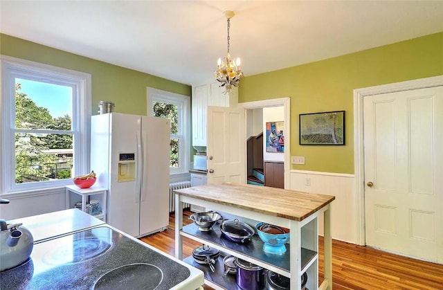 kitchen with white refrigerator with ice dispenser, radiator heating unit, a chandelier, wood finished floors, and wainscoting