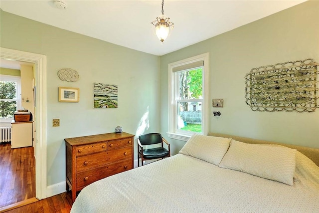 bedroom with multiple windows, radiator, dark wood-style floors, and baseboards