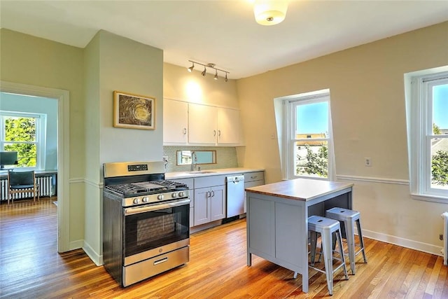 kitchen with stainless steel gas range, light wood finished floors, dishwashing machine, rail lighting, and plenty of natural light