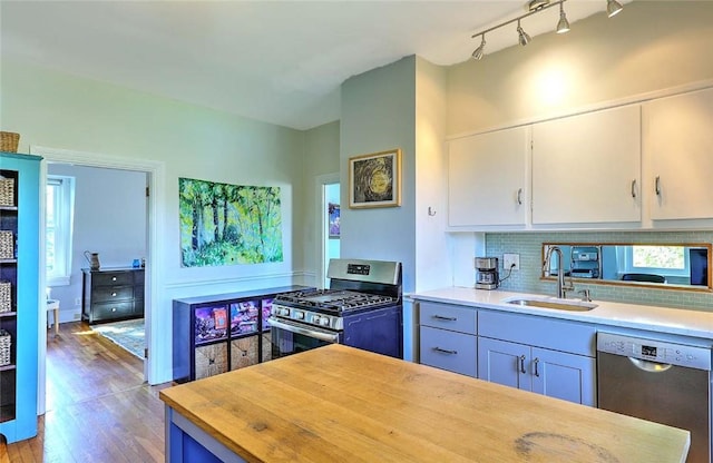 kitchen featuring a sink, appliances with stainless steel finishes, wood finished floors, decorative backsplash, and white cabinetry