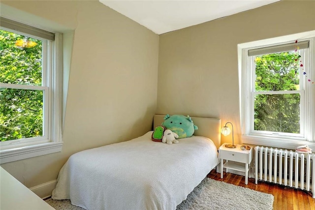bedroom with radiator heating unit, wood finished floors, and baseboards