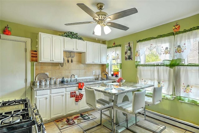 10 Westcott Ave Unit 3, Boston, MA 02124 - kitchen with gas range, a baseboard heating unit, white cabinets, decorative backsplash, and ceiling fan