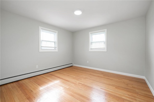 spare room with a baseboard radiator, healthy amount of natural light, light wood-style floors, and baseboards