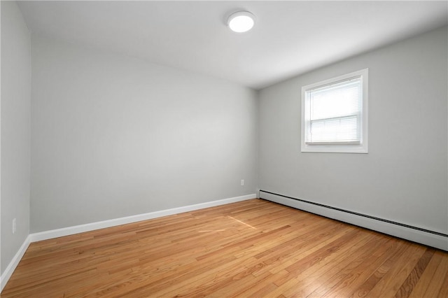 spare room featuring baseboard heating, light wood finished floors, and baseboards