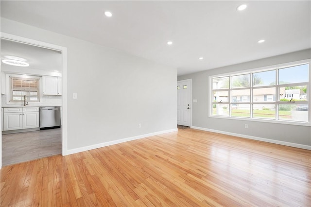 unfurnished living room with baseboards, light wood-style flooring, a sink, and recessed lighting