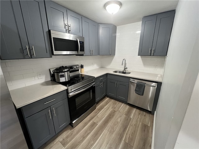 kitchen with stainless steel appliances, a sink, light wood-style floors, light countertops, and decorative backsplash