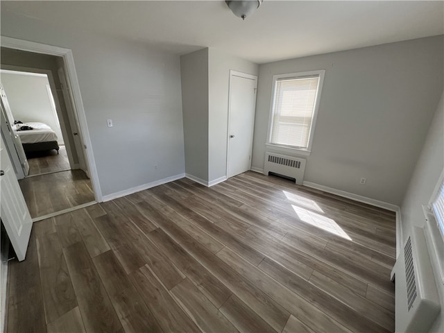 unfurnished bedroom with radiator, dark wood-type flooring, baseboards, and a closet