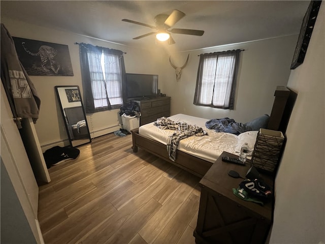 bedroom with a baseboard heating unit, wood finished floors, and ceiling fan