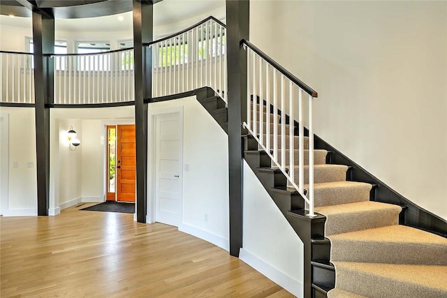 stairway featuring plenty of natural light, wood finished floors, a high ceiling, and baseboards
