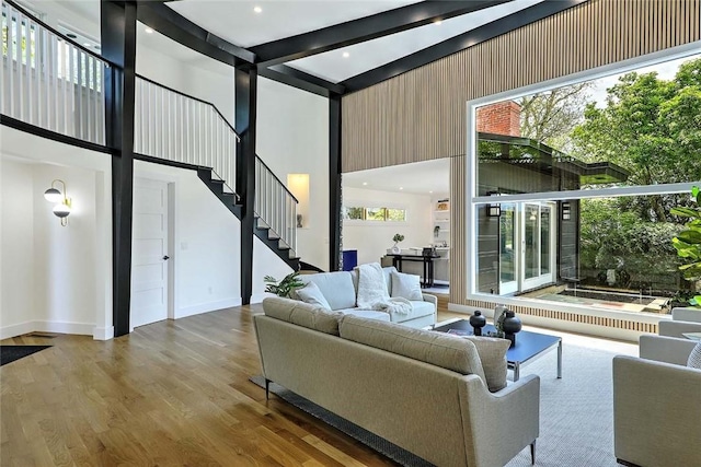 living area with a high ceiling, beam ceiling, stairway, wood finished floors, and baseboards