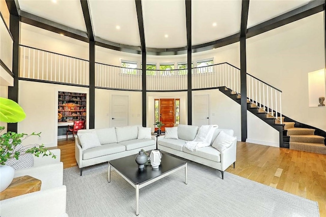 living area featuring wood finished floors, a towering ceiling, stairs, beam ceiling, and baseboards