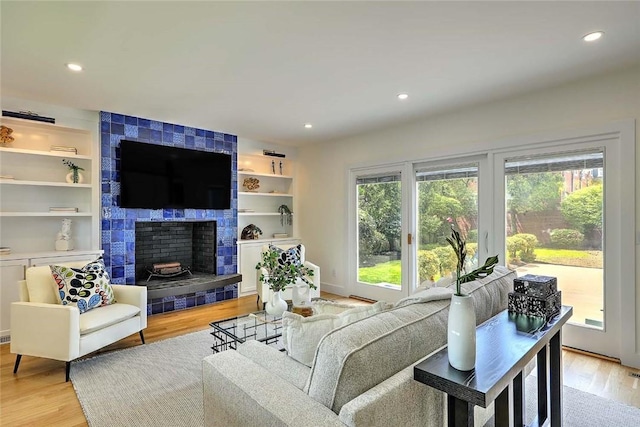 living area featuring a tile fireplace, light wood-type flooring, recessed lighting, and built in features