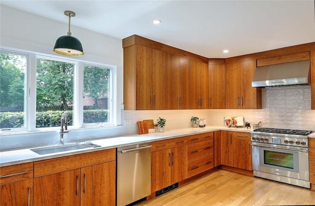 kitchen with appliances with stainless steel finishes, wall chimney range hood, a sink, light countertops, and recessed lighting