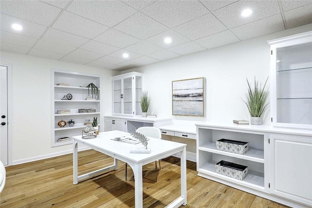 office featuring light wood finished floors, recessed lighting, built in shelves, a drop ceiling, and baseboards