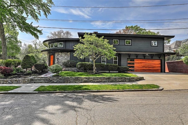 contemporary house with an attached garage, concrete driveway, and stone siding