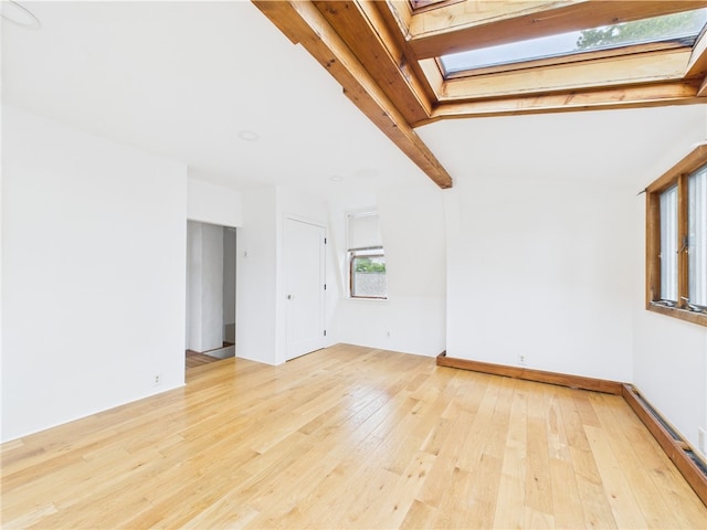 unfurnished room with a skylight, light wood-style floors, and beam ceiling