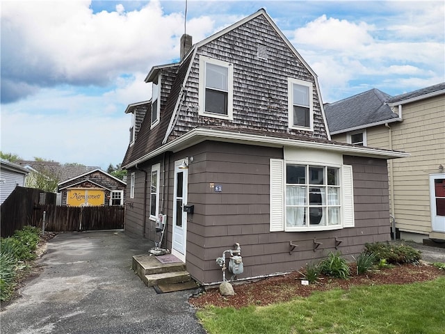 view of front of home with fence, a chimney, a gambrel roof, and driveway
