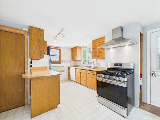 kitchen featuring gas stove, wall chimney range hood, dishwasher, light floors, and a sink