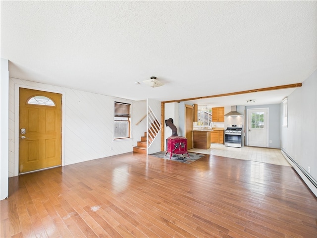 living area featuring light wood-style flooring, stairway, a baseboard heating unit, and a textured ceiling
