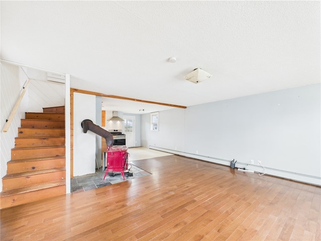 unfurnished living room featuring a wood stove, wood finished floors, and stairway