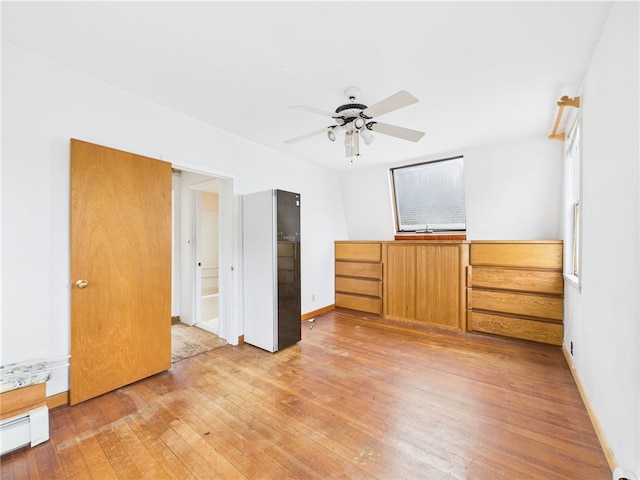 unfurnished bedroom with a baseboard heating unit, light wood finished floors, and baseboards