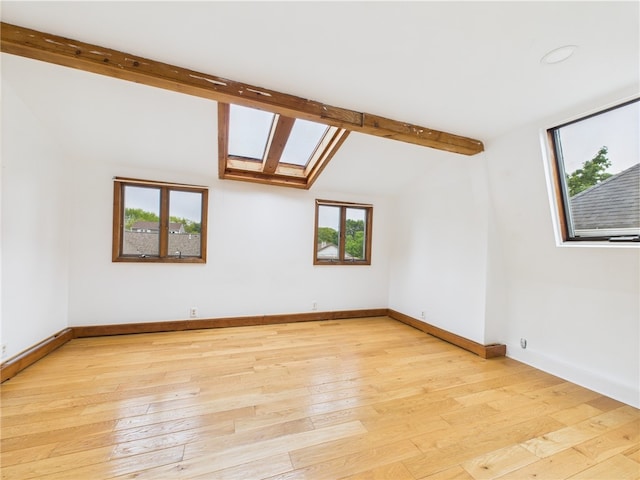 spare room with a skylight, light wood-style floors, and baseboards