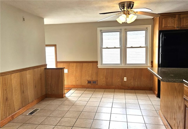 unfurnished dining area featuring wainscoting, ceiling fan, plenty of natural light, baseboards, and light tile patterned flooring