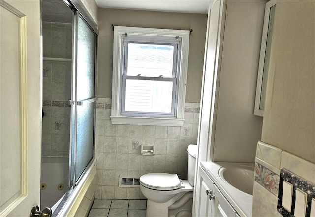 bathroom with tile patterned flooring, tile walls, toilet, vanity, and a wainscoted wall