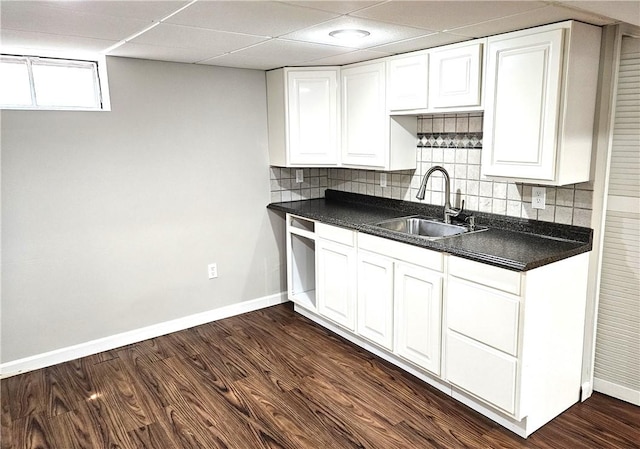 kitchen featuring a sink, dark countertops, baseboards, decorative backsplash, and white cabinetry