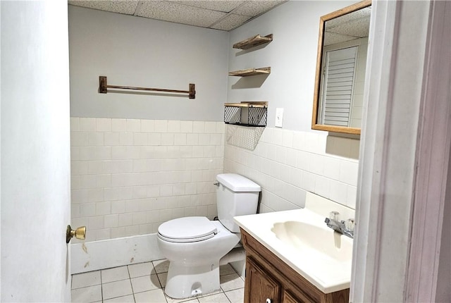 bathroom with tile patterned floors, toilet, tile walls, vanity, and a paneled ceiling