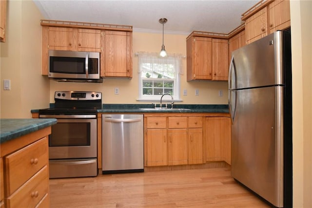kitchen featuring appliances with stainless steel finishes, a sink, dark countertops, light wood-style floors, and ornamental molding