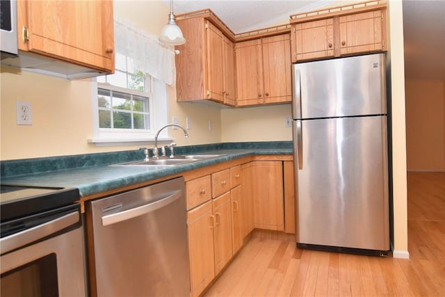 kitchen featuring stainless steel appliances, a sink, light wood finished floors, dark countertops, and pendant lighting