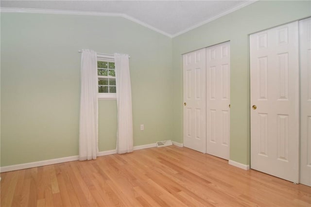 unfurnished bedroom featuring crown molding, light wood-style flooring, baseboards, lofted ceiling, and multiple closets